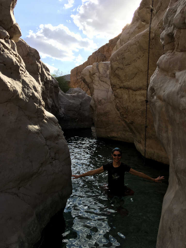Malina up to her belly in water in a very narrow pool between high rocks near Miqil, Oman.